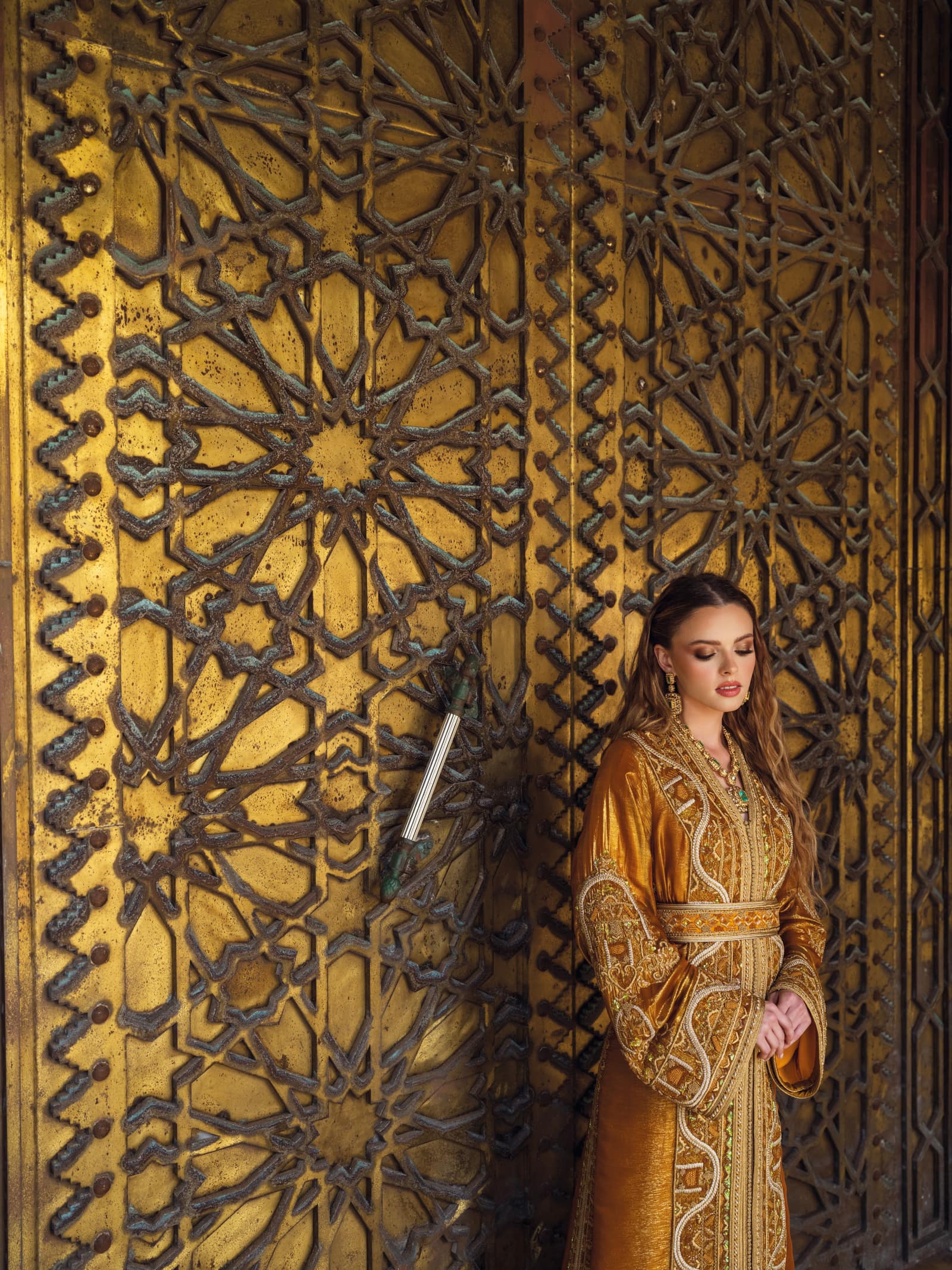 Bronze Moroccan caftan beside ornate golden door with green embroidery accents