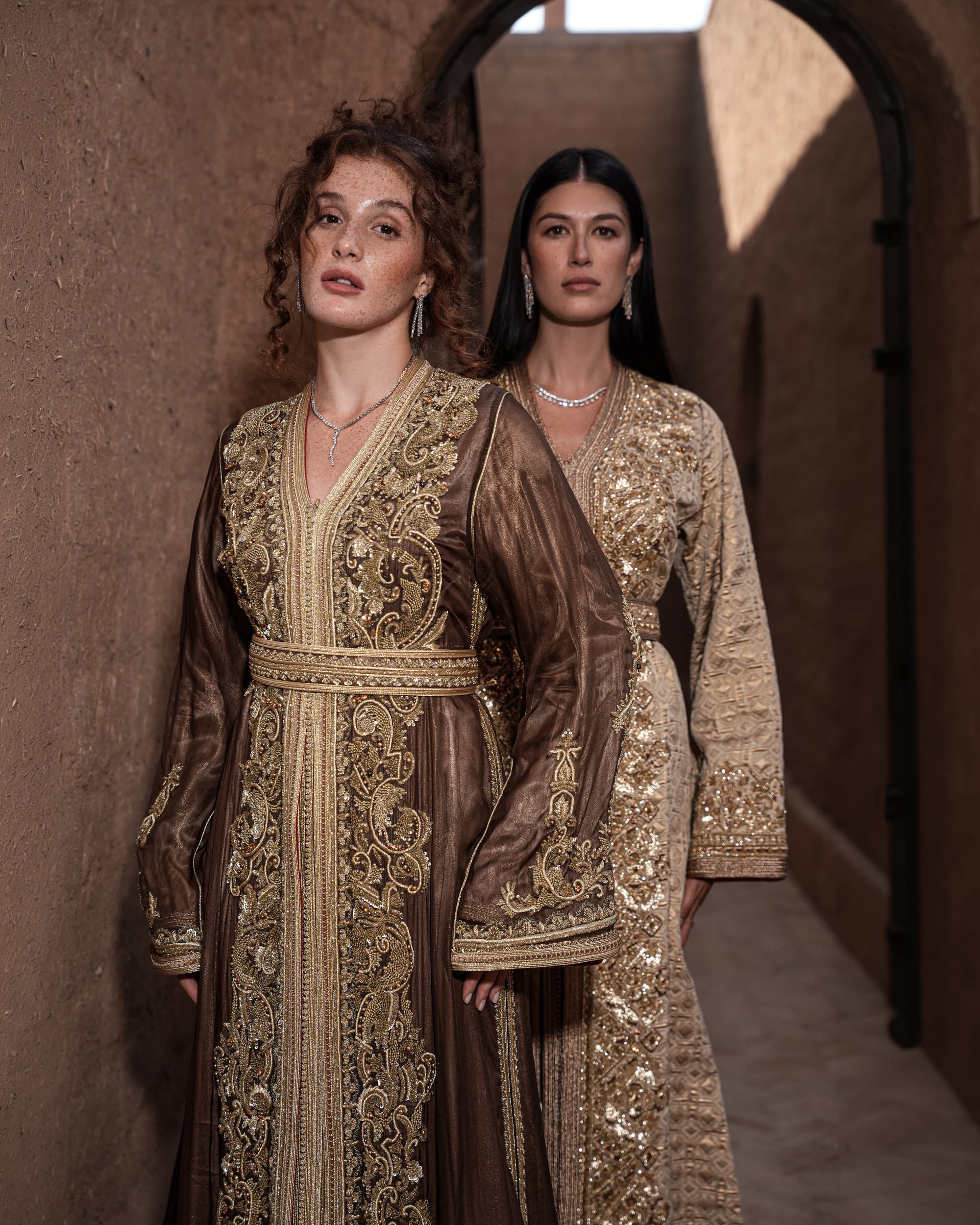 Bronze Reverie lamé organza Moroccan kaftan with gold embroidery, worn open over a champagne dress, shown alongside a second look