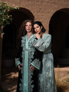 Cypress Portico deep green velvet Moroccan kaftan with sea-green embroidery, shown alongside a second look